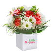 There's an uplifting energy woven into this Motspur Park bouquet, as if the joy of a local spring morning has been gathered and artfully arranged. Nestled in a crisp white gift bag with sturdy ribbon handles, each flower is thoughtfully placed: coral and peach carnations, lavishly ruffled, unfold alongside bright white daisies whose yellow-green centers shine like the fresh grass after rain. Wisps of baby's breath, airy and delicate, float among the main blooms, echoing the gentle clouds above Motspur Park Recreation Ground. Purple-tinged buds and unopened flowers peep out from the left, offering subtle intrigue. The entire bouquet is cradled by deep green, glossy foliage, arching gracefully to provide structure and depth. The clean white background and expert composition highlight each colour and texture, making the bouquet feel as radiant and sincere as a smile from a neighbour on a walk along Balmoral Avenue. Perfect for delivering cheer on a birthday, sending love for an anniversary, or simply brightening someone's day, this lush arrangement represents the best of Motspur Park floristry-fresh, locally inspired, and presented with the care only a true neighbourhood florist can provide.
